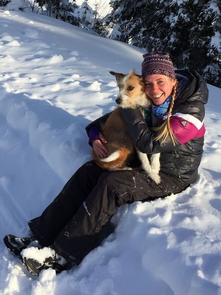 Eine Frau sitzt im Schnee neben ihrem Hund und genießt die winterliche Landschaft.